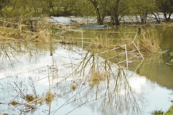 überflutete Lahnaue in Marburg-Wehrda. Im Hintergrund die fließende Lahn, davor die Baumlinie als Markierung des Ufers. Ein Kanu treibt Kiel oben iim Überflutungsgebiet. hohe trockene Gräser ragen aus dem Wasser. Ein Weidezaun spiegelt sich im Wasser. Hier stehen für gewöhnlich die Pferde in Pflege des hiesigen Veterinärs.