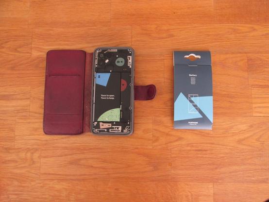 The backcover has been removed and the phone has been placed upside down in the case (to avoid screen scratches). The battery in its wrapper still to the right.