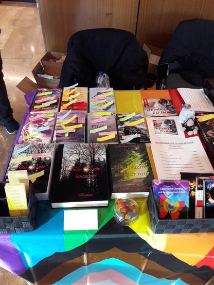 At a book fair: Several books with memos and promotion material on a table with a Pride flag.