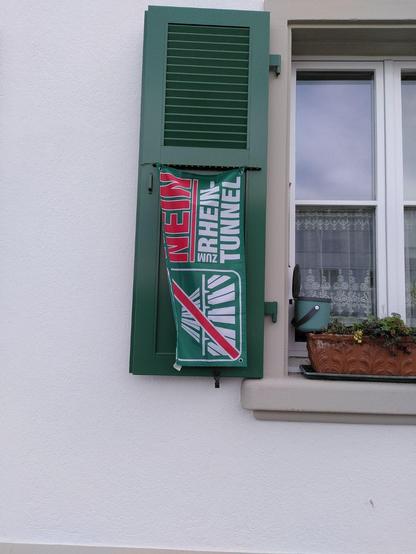 Fahne mit dem Text "Nein zum Rheintunnel" an einem Fensterladen bei einem Küchenfenster