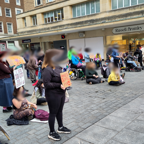 Around 40 people, some of them visibly using mobility aids, stand in Exeter's Bedford Square holding signs and placards protesting the cuts