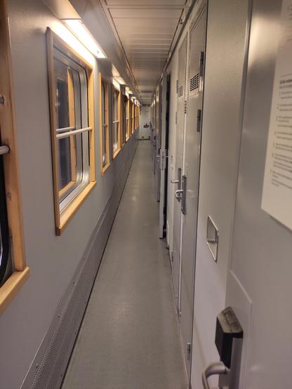 A train corridor with a line of windows down the left side and a line of doors down the right.