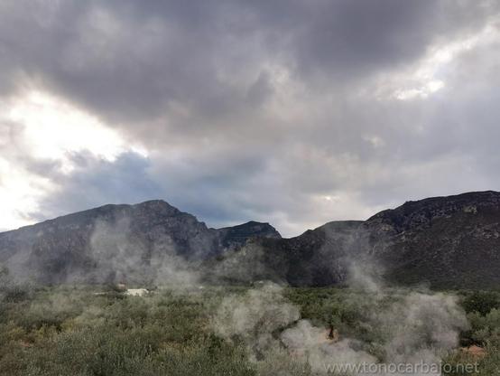 Montañas, nubes olivar y un poco de humo de la chimenea en primer plano