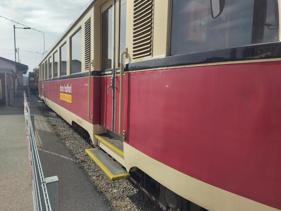 Ein Triebwagen der Vorchdorferbahn, fotografiert von schräg außen, sodass nur die Seite, nicht jedoch die Front zu sehen ist. Beige lackiert, mit einem breiten roten streifen quer über den Zug, mit Firmenschriftzug Stern+Hafferl Verkehr.