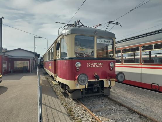 Det gleicke Triebwagen, von schräg vorne fotografiert. Vorne beschriftet mit "Salzburger Lokalbahn" und der Nummer 32. Hinter der Windschutzscheibe ein Schild "Lambach".