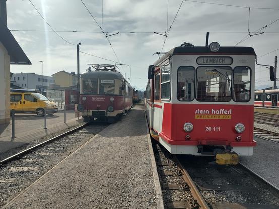 Zwei Triebwägen der Vorchdorferbahn, frontal fotografiert. Der linke davon ist der bereits im vorigen Bild gezeigte. Rechts daneben ein etwas neuer wirkender, ebenfalls mit einem Schild für "Lambach" in der Zielanzeige. Vorne der "Stern+Hafferl Verkehr" Firmenschriftzug sowie die Nummer 20 111 auflackiert.