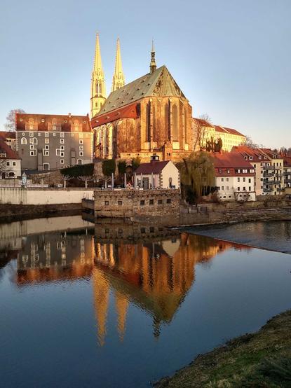 Die Kirche Sankt Petri und Paul in Görlitz spiegelt sich im Morgenlicht in der ruhig fließenden Neiße.