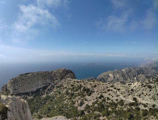 Vue depuis le Cap Gros (509m) plein sud.

En contrebas, on voit le "dos" de la Candelle, tel un gros boudin de calcaire, c'est une impressionnante falaise déjà de ce côté alors que de l'autre elle est encore plis grande.
Pour y arriver on voit une pente avec de la végétation et un chemin de randonnée qui se dessine jusqu'au col de la Candelle.

Sur la droite (vers l'ouest) les enchaînements de caps dessine les calanques de Marseille. La vue est imprenable et s'étend loin.

En reine, la mer est bien visible sur toute la largeur de la photo.

Et au loin au milieu, on peut voir l'ile de Riou.