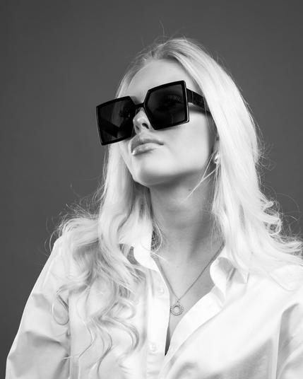 Black and white studio portrait of a woman wearing oversized fashion sunglasses and a white shirt, with one hand in her hair – shot by Kuvaajankulma in Lappeenranta