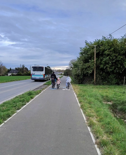 Une famille de trois, à vélos, sur le REV. Le père de famille pousse sa jeune fille à vélo. Le plus grand roule à leurs côtés.