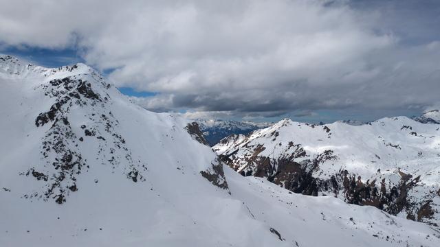 White and dark clouds with some deep blue spots in the sky over snowy mountains.