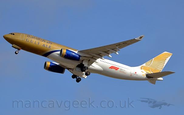 Side view of a twin engined jet airliner flying from right to left at a low altitude, with undercarriage being stowed away, flaps extended from the rear of the wings, and the nose raised very sharply, suggesting it has just taken off.
The plane is painted gold at the front and white at the back, with a purple band around the lower fuselage just forward of the wing.
The tail is filled with a large image of a golden stooping falcon, a design that is replicated in a much smaller form on the upturned wing tips..
The engine pods are purple, with gold inlets.
The registration "A9C-KD" is painted on the underside of the outer section of the left wing.
There is a large, red "F1" logo on the lower rear of the fuselage.
Blue sky with the odd wisp of grey cloud fills the rest of the frame.
