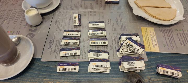 Barcode tokens arranged in batches of ten. Some piles are groupef in hundreds. They are on a cafe table with drinks and food around them.