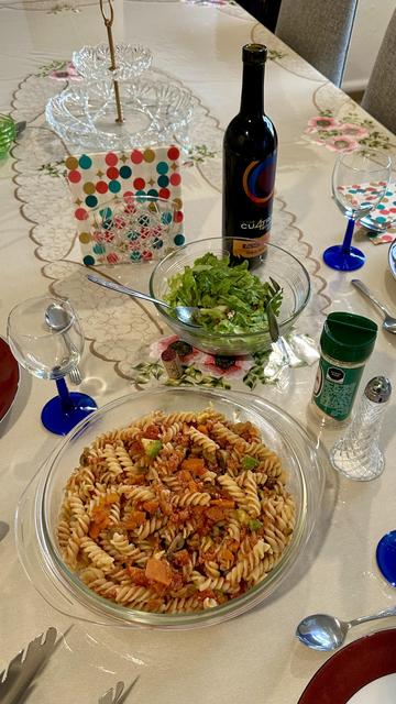 Photo of a table with a bowl of pasta, salad, and a bottle of wine
