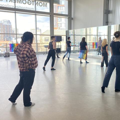 A teacher in a circle of students demonstrates back extension of the left leg, and some students try it too.