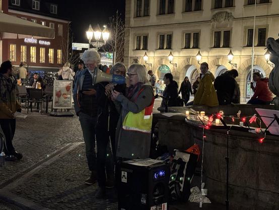 Eine Person macht mit einem Megafon eine Ansage in Richtung der Teilnehmer:innen.