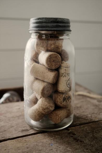 En glasburk med lock i grå metall. Burken innehåller vin- och champagnekorkar. Den står på en trären yta och är belyst av naturligt ljus från vänster.