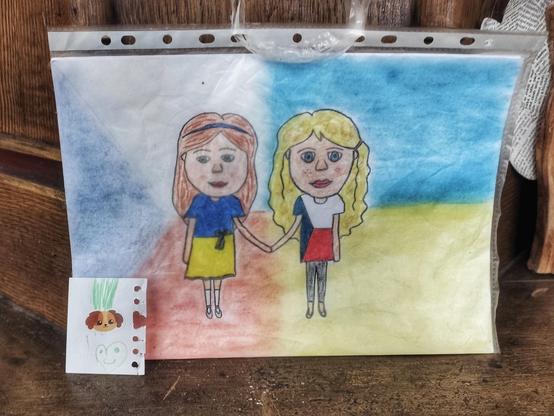 Foto eines Kinderbildes in der tschechischen Kirche St. Nikolaus und St. Elisabeth in Cheb, das zwei Mädchen zeigt, die in den Farben der Tschechischen Republik und der Ukraine gekleidet sind und sich an den Händen halten. Im Hintergrund noch einmal die Farben der ukrainischen und tschechischen Fahnen.