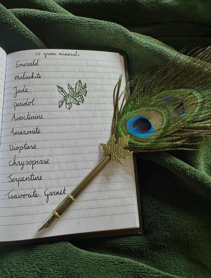 Notebook on a green blanket, peacock feather dip pen, cursive text in green ink. 

10 green minerals. 

Emerald
Malachite
Jade
Peridot
Aventurine
Dioptase
Chrysoprase
Serpentine
Tsavorite Garnet
