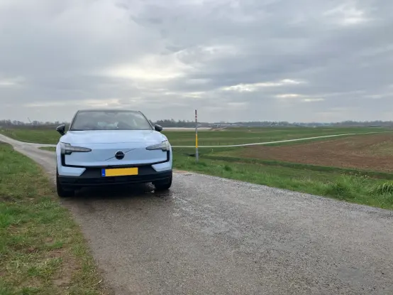 A cloud blue Volvo EX30 parked on a dike road; panoramic head on front view.