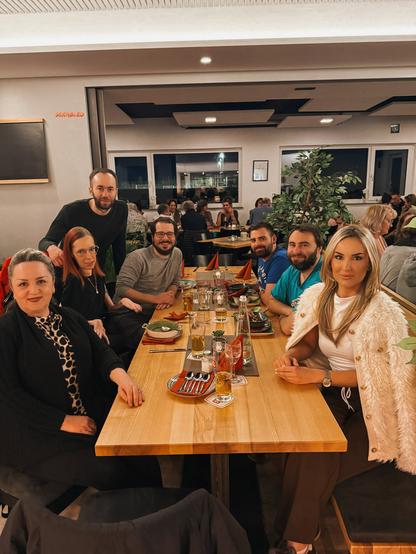 Mein Team und einige Freunde sitzen an einem Holztisch im Anno 55 in Forstinning. Im Vordergrund sitzen Zerina und Slavica, dann Darius und ich, Mesud steht hinter mir, dann folgen Heft und Jakob. Auf dem Tisch stehen einige Teller und Gläser.