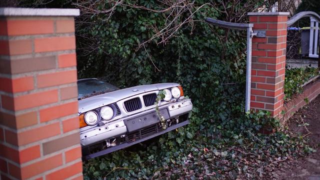 sehr schräge Einfahrt, eine Front eines alten BMW guckt heraus, Latten am Zaun auch längst alle verschwunden