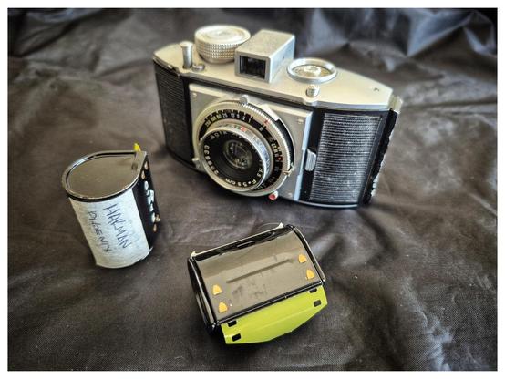 A vintage Agfa Karat camera on a crumpled black background (my dark bag). In front are two Rapid canisters loaded with Harman Phoenix film.