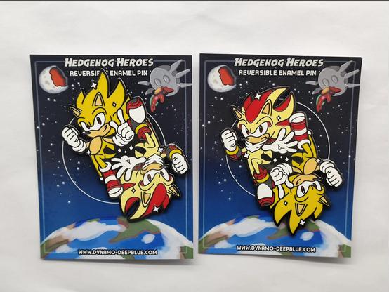 A photograph of two enamel pins with a design featuring Super Sonic and Super Shadow. The pin design itself shows Sonic and Shadow floating opposite each other, each with one leg raised and bent, in a yin-yang sort of fashion, with a heroic air. Because of this, the design is reversible, so one can face right side-up while the other faces upside-down. The photo shows one pin facing one direction and a second pin beside it facing the opposite direction.

Sonic is looking toward the viewer with a confident smirk while Shadow looks toward the viewer with a stoic frown. They both have their right hand clenched into a fist, but Sonic is doing his signature finger wag while Shadow holds hand out forward with his fingers splayed, with their left hands. Sonic is also wearing his SOAP shoes from Sonic Adventure 2 rather than his regular shoes.

The backing card design has a starry space background with Earth in view towards the bottom. The Eclipse Cannon floats in the upper right hand corner of the image, with the Biolizard/Finalhazard attached to the front of the structure. The upper left shows the moon razed in half by the Eclipse Cannon.