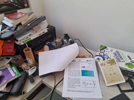 Fotografia de uma mesa com bastante entropia destacando uma prova de física aberta