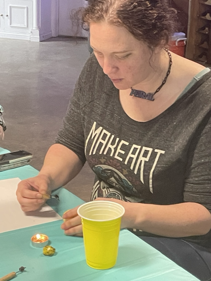 A woman writing pysanky eggs. With a blue table cloth with egg, candle, kitskas and a yellow cup