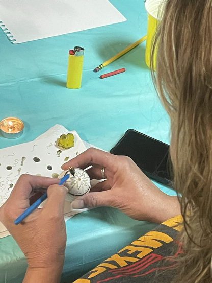 A woman writing pysanka with a candle and wax on a blue table cloth.