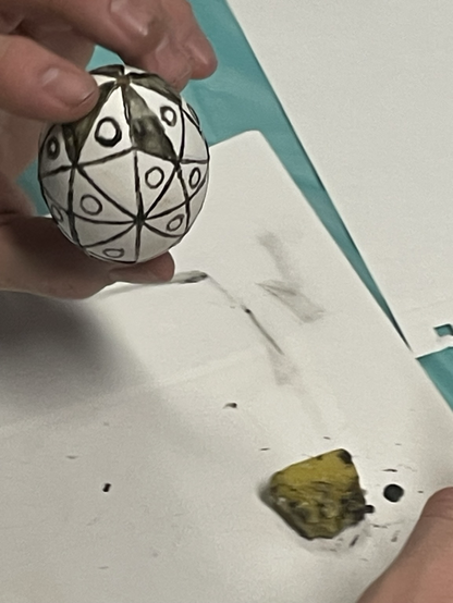 A man holding the pysanka he is working on with triangles,lines and circles with wax.