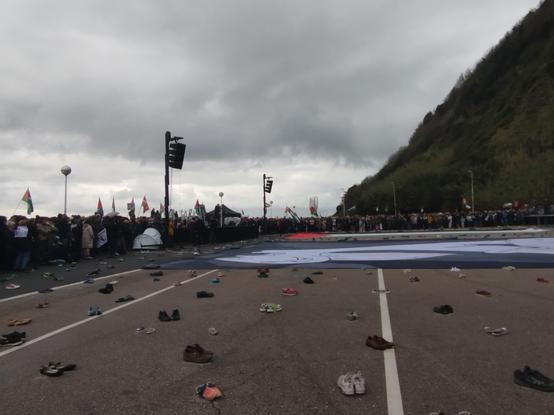 Manifestazioaren amaiera Sagueseko plazan, jendea eszenatoki aurrean lurrean dauden palestina eta Gernikako bandera erraldoiak inguratzen. Lurrean zapata eta zapatila paretak, jaberik gabe.