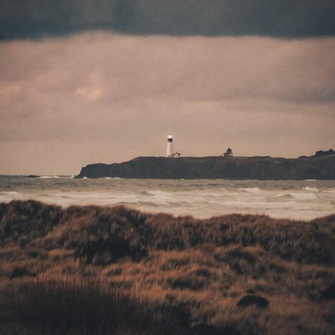 Photo shows a stormy day on the Oregon Coast with a light house in the distance