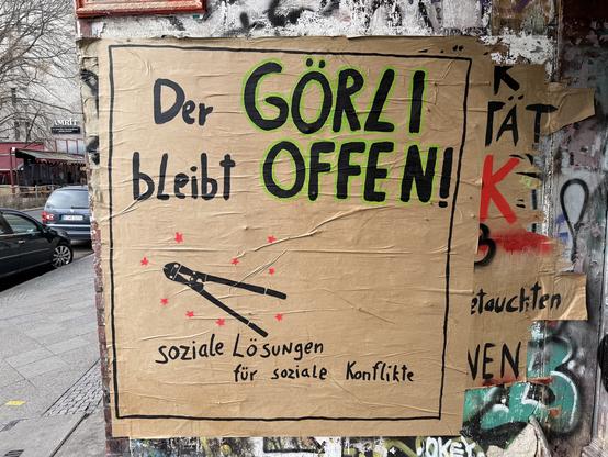 Plakat an einer Hauswand, darauf steht: Der Görli bleibt offen! Soziale Lösungen für soziale Konflikte. In der Mitte ein Bild von einem Bolzenschneider.