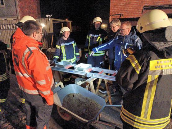 Eine Diskussion zwischen Feuerwehr und THW über die Vor- und Nachteile der Trichter am Versuchsaufbau, ich stehe auch dabei und eine Schubkarre Sand.