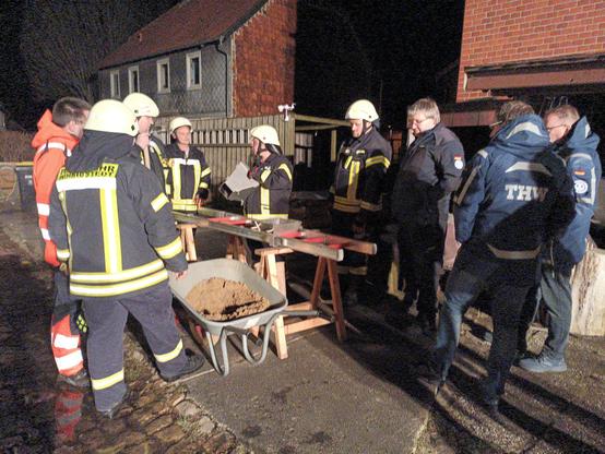 Feuerwehrleute probieren den Sandsack-Fülltrichter aus, daneben stehen drei THW-Helfer und ich bin auch da.