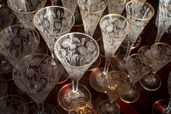 Array of clear glassware covered with floral etchings and rimmed in gold.