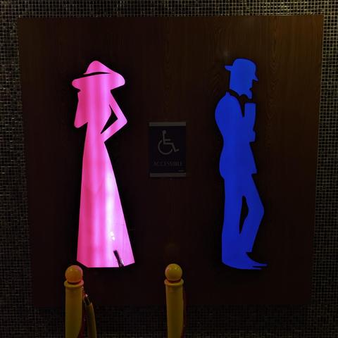 Two gender markers indication bathroom sections for men/women.
Left side, tall pink coloured silhouette of a woman
Right side, equally tall blue coloured silhouette of a man (or in my joke, a masculine woman)