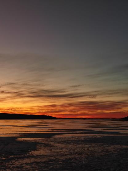 Orange sunset at a frozen lake. Sky has some clouds which are a bit darker and the ice reflects sunsets colors.
