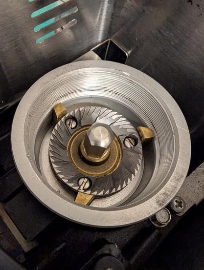Photo showing the insides of a burr coffee grinder: the aluminium burr is held in a brass cradle and secured in place with a central stainless steel bolt.