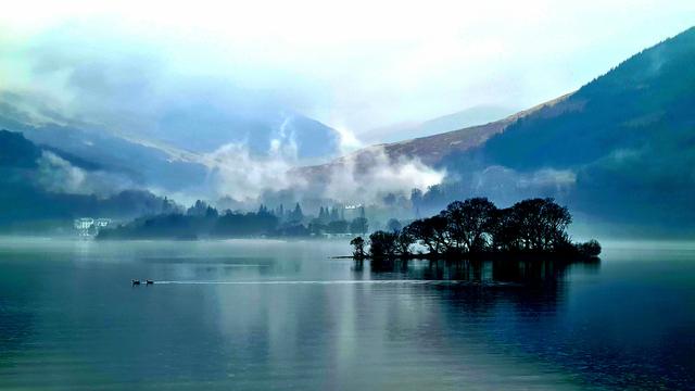 Looking across a calm Scottish loch towards the misty hills on the opposite side.