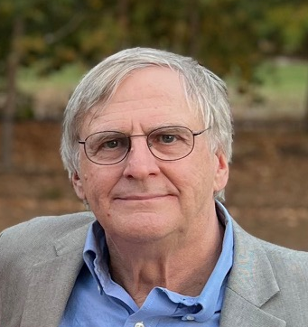 Portrait of the author of the guest commentary in Radio World, Kim Andrew Elliott. A headshot of an older, white male person with glasses, a blue shirt and a grey jacket.