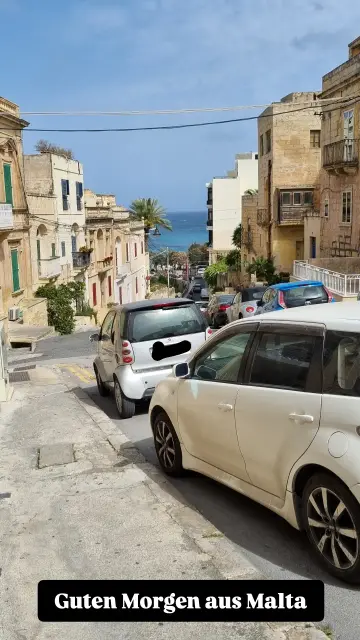 Foto einer Straße im Norden Maltas, die zum Meer führt. Häuser und Autos auf beiden Seiten der Straße.