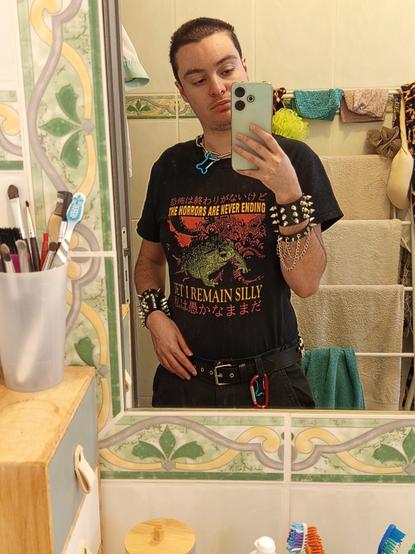 Moi en photo dans la salle de bain, t-shirt noir crapaud, chaine collier os, bracelet noir clous, ceinture noire et mousqueton rouge.