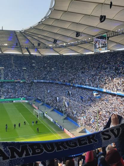 Das Bild zeigt die vollbesetzte Nordtribüne im Volksparkstadion. Man sieht ein Meer aus hochgehaltenen Fanschals kurz vor Spielbeginn, dazwischen einige große Schwenkfahnen. Im Vordergrund ist auf einem hochgehaltenen Schal der Schriftzug Hamburger SV zu lesen.