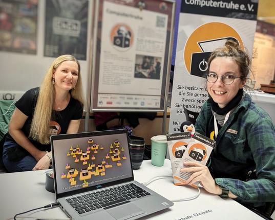 Bild zeigt Annette und Karola am Stand der Computertruhe Chemnitz auf den Linuxtage., im Vordergrund Laptop mit dem Computertruhe Erklärfilm.