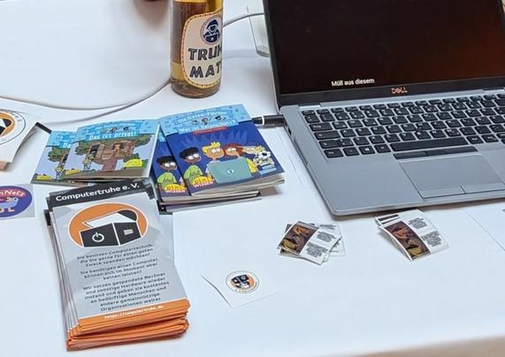 Bild zeigt Macro auf den Stand mit Computertruhe Flyern, Stickern und Laptop