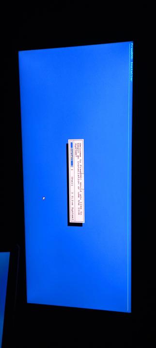 The photograph shows a computer screen displaying the FreeBSD installer interface. The background is a solid blue color, and the text is primarily in white and red. On the right side of the screen, the text "FreeBSD Installer" is visible in white. In the center, there is a white rectangular box with red text that reads "Welcome to FreeBSD. Would you like to install or use the live system?" Below this, there are three options listed vertically: "Install," "Shell," and "Live System." The cursor is positioned next to the "Install" option. The overall layout is simple and straightforward, with a focus on the installation options.
