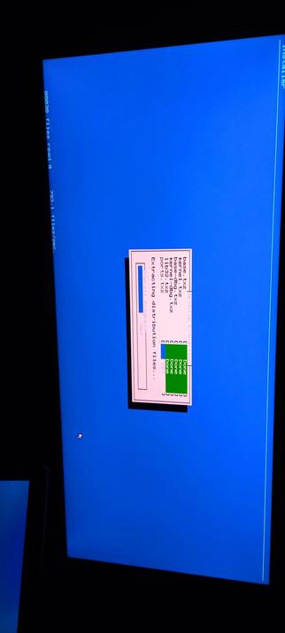 The photographic composition shows a computer screen with a blue background. In the center, there is a pink rectangular box with a black border containing text and a progress bar. The text reads "Extracting distribution files..." and lists several file types being extracted, including "base.txz," "kernel-dbg.txz," "kernel.tgz," "ports-txz," and "11p32-txz." The progress bar is partially filled with a green section labeled "Done," indicating the extraction process is ongoing. The screen also displays vertical text on the left side, reading "88830 files read" and "793.1 files/sec." The cursor is visible as a small white arrow in the bottom left corner of the screen.